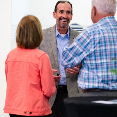 Woman in a coral jacket and a man in plaid talking with a smiling man in a tweed blazer