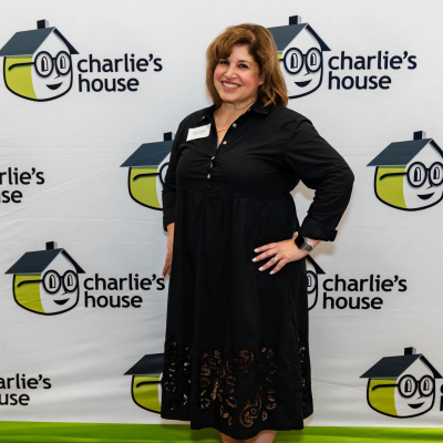 Smiling woman in a black dress posing at the Charlie's House photo backdrop