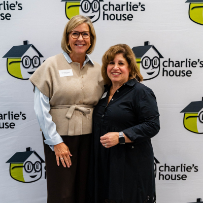 Two women posing together in front of the Charlie's House logo wall
