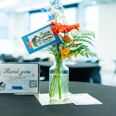 Table centerpiece of orange and blue flowers with a Charlie's House 5 year tag and thank you card