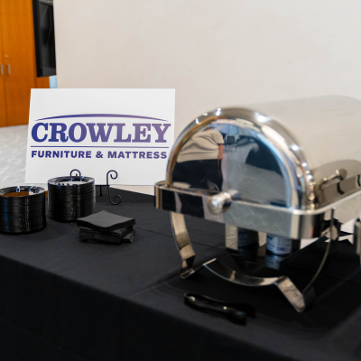 Buffet chafing dishes beside a Crowley Furniture & Mattress sponsor sign