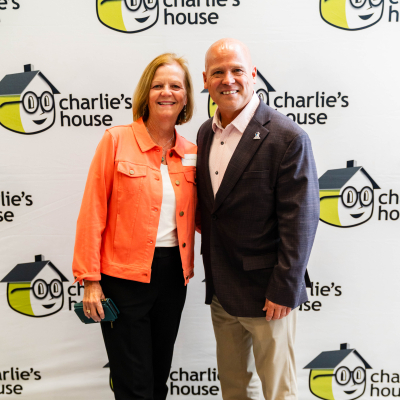 Woman in an orange jacket posing with a man at the Charlie's House backdrop