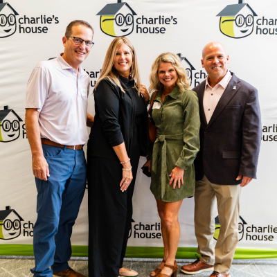 Two couples posing together in front of the Charlie's House banner