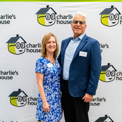 Couple posing at the Charlie's House backdrop, the woman in a blue floral dress