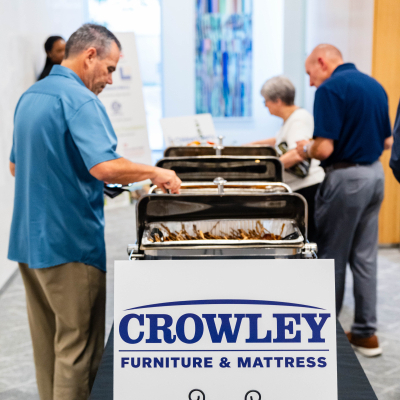 Guest filling a plate at the buffet behind a Crowley Furniture & Mattress sign
