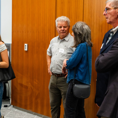 Small group of guests talking near a wood-paneled wall