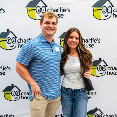 Young couple smiling for a full-length photo at the Charlie's House backdrop