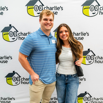 Young couple posing together in front of the Charlie's House logo wall