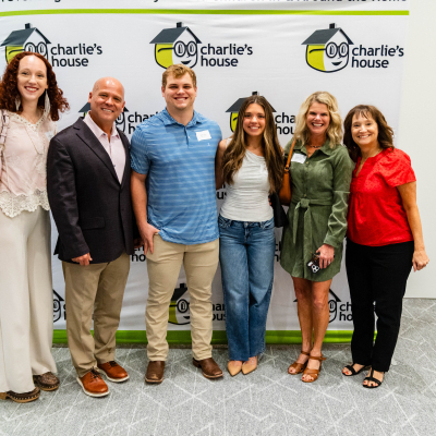 Six guests smiling for a group photo at the Charlie's House backdrop