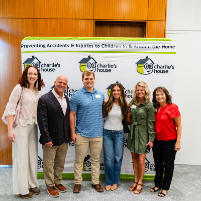 Group of six guests posing together in front of the Charlie's House banner