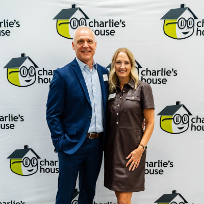Couple posing at the Charlie's House backdrop, the man in a navy suit