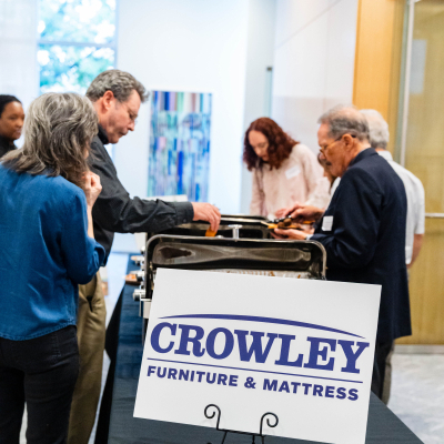 Guests at the buffet table behind a Crowley Furniture & Mattress sponsor sign