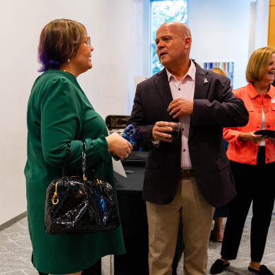 Man in a dark blazer chatting with guests while holding a drink