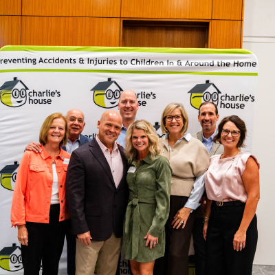Group of eight guests posing together in front of the Charlie's House banner