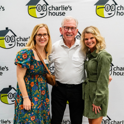 Three guests posing for a full-length photo at the Charlie's House backdrop