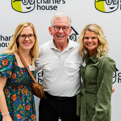 Older man posing with two women at the Charlie's House photo backdrop
