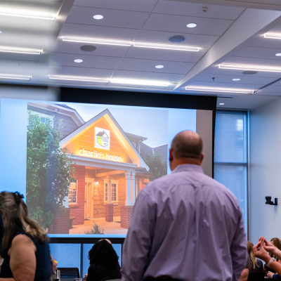 Guests gathering in the event room with a photo of a house on the screen