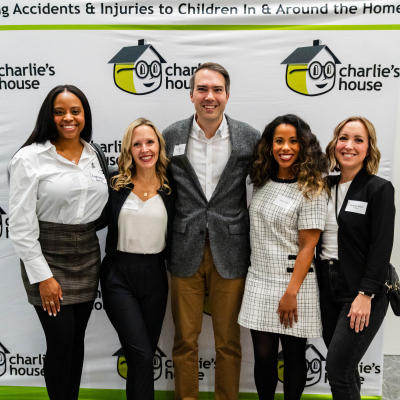 Group of five guests posing for a full-length photo at the Charlie's House banner