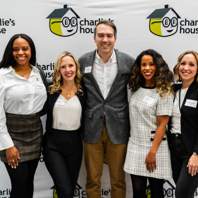 Five guests smiling together in front of the Charlie's House logo wall