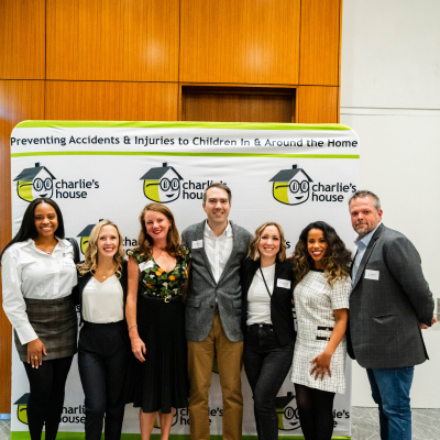 Group of seven guests standing in front of the Charlie's House banner
