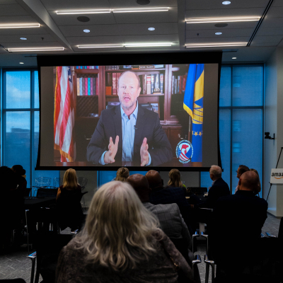 Guests watching a video message from a man seated in front of flags