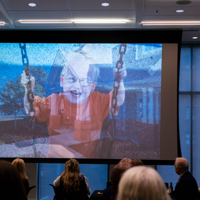 Audience watching a large screen showing a young child smiling on a swing