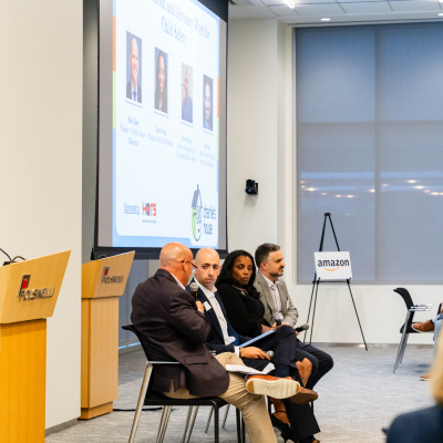 Four panelists seated at the front of the room beneath a presentation screen