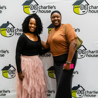 Two women posing together in front of the Charlie's House banner