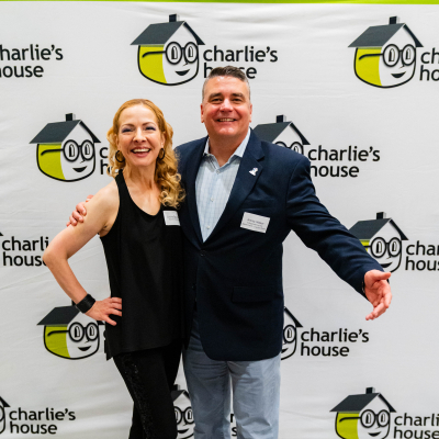 Man with arm outstretched posing with a woman at the Charlie's House backdrop