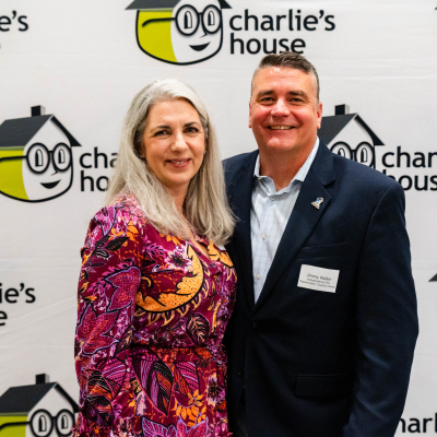 Smiling couple posing in front of the Charlie's House logo wall