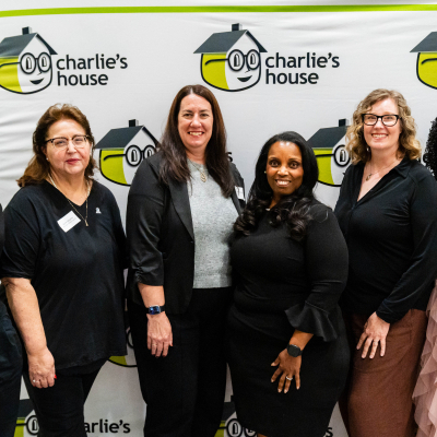 Six smiling women standing together at the Charlie's House photo backdrop