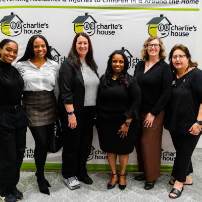 Group of six women posing in front of the Charlie's House banner