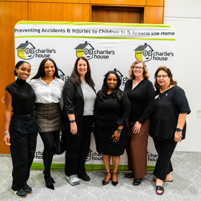 Six women posing together in front of the Charlie's House Preventing Accidents & Injuries banner