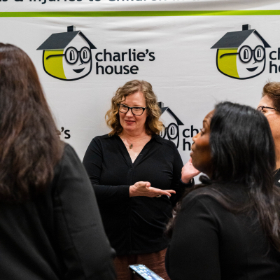 Woman in glasses chatting with guests at the Charlie's House backdrop