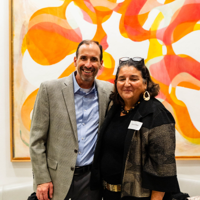 Man and woman smiling in front of a colorful orange abstract painting