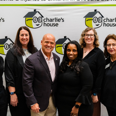 Smiling group photo in front of the Charlie's House Preventing Accidents & Injuries banner