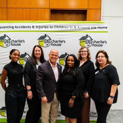Group of six guests dressed in black posing at the Charlie's House banner