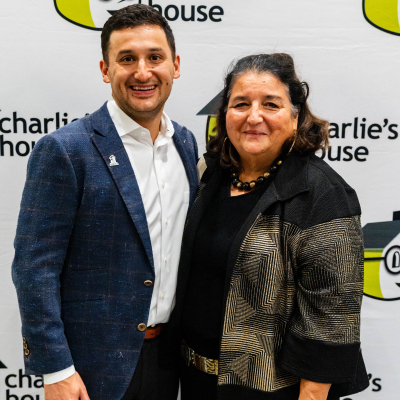 Smiling man and woman standing together in front of the Charlie's House logo wall