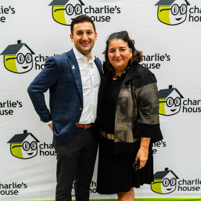 Man in a navy blazer and a woman posing at the Charlie's House backdrop