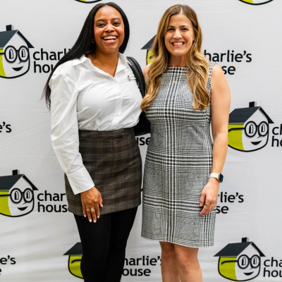 Two women standing together in front of the Charlie's House backdrop