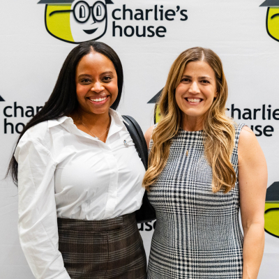 Two smiling women posing at the Charlie's House photo backdrop