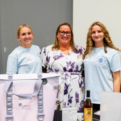 Three smiling volunteers at the raffle table with prizes and ticket bowls