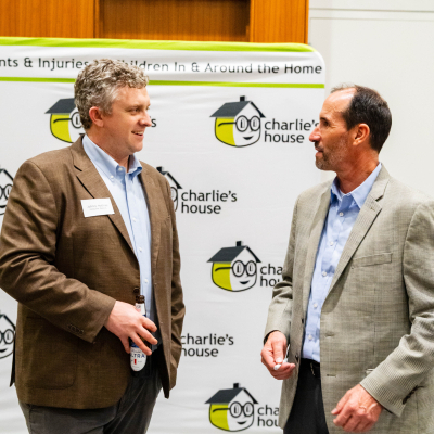 Two men talking in front of the Charlie's House banner