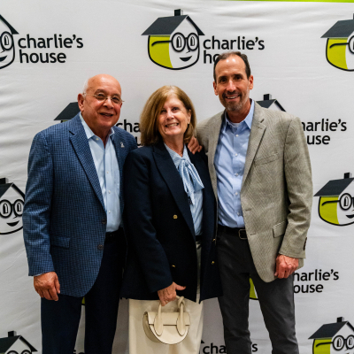 Two men and a woman posing for a full-length photo at the Charlie's House backdrop