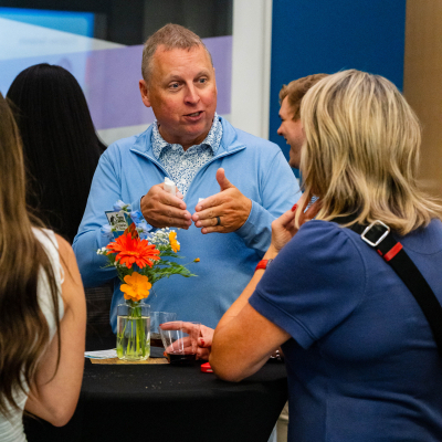 Man in a blue sweater talking with guests at a cocktail table