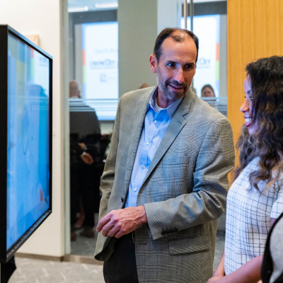 Man in a gray blazer listening to guests beside the interactive safety display