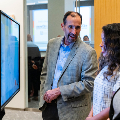 Man in a tweed blazer speaking with two women next to the touchscreen display