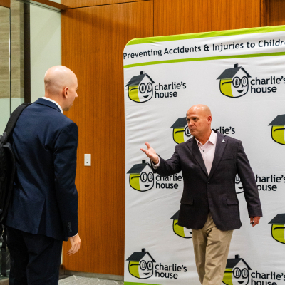 Man in a dark blazer waving a guest over to the Charlie's House photo backdrop