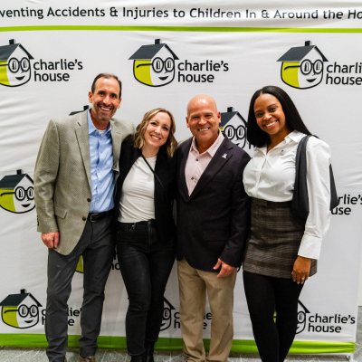 Four guests posing for a full-length photo at the Charlie's House banner