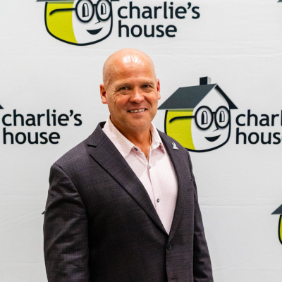 Portrait of a smiling man in a dark blazer in front of the Charlie's House logo wall